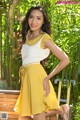 A woman in a yellow skirt posing on a wooden bench.